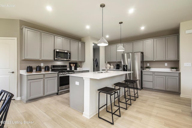 kitchen with gray cabinetry, a kitchen island with sink, hanging light fixtures, sink, and appliances with stainless steel finishes