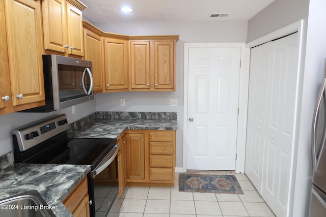 kitchen with appliances with stainless steel finishes, light tile patterned floors, and dark stone countertops