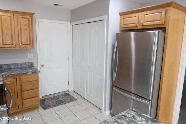 kitchen with stainless steel fridge, light tile patterned flooring, and dark stone countertops