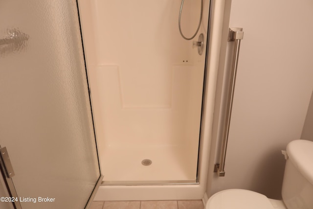 bathroom with tile patterned floors, toilet, and a shower with door