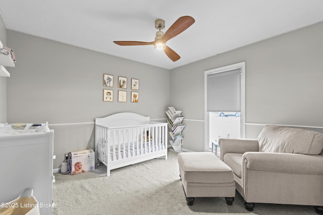 carpeted bedroom with ceiling fan and a crib