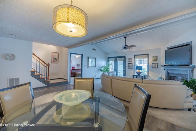 dining space featuring ceiling fan, lofted ceiling with beams, wood-type flooring, and a textured ceiling