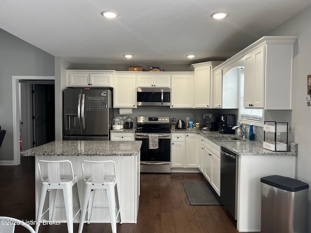 kitchen with appliances with stainless steel finishes, sink, white cabinets, dark hardwood / wood-style flooring, and light stone countertops