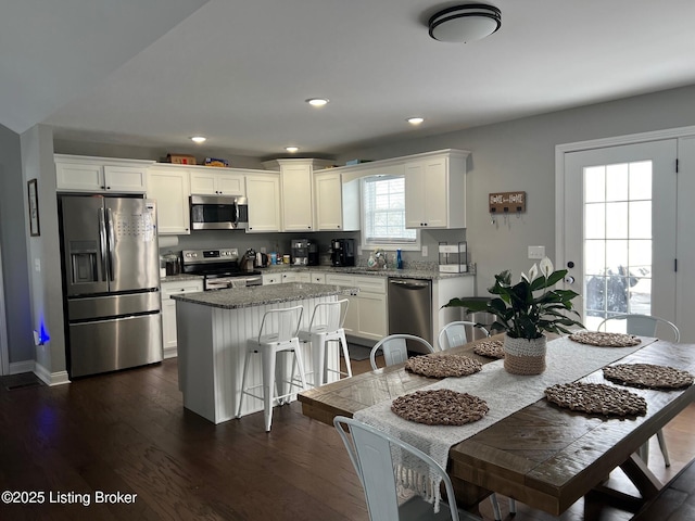 kitchen featuring a breakfast bar, appliances with stainless steel finishes, a kitchen island, light stone countertops, and white cabinets