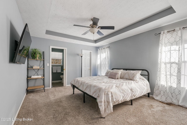 carpeted bedroom with a raised ceiling, connected bathroom, ceiling fan, and a textured ceiling