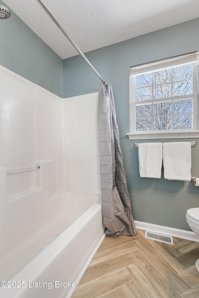 bathroom featuring toilet, parquet flooring, a textured ceiling, and shower / tub combo with curtain