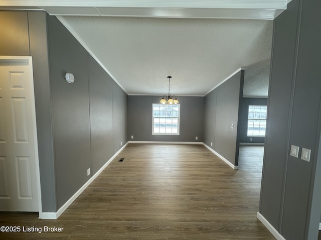 unfurnished dining area featuring an inviting chandelier, crown molding, dark wood-style flooring, and a textured ceiling