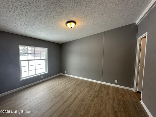 empty room featuring a textured ceiling, baseboards, and wood finished floors