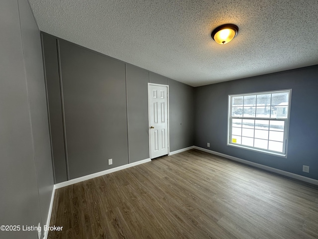 unfurnished room with vaulted ceiling, wood finished floors, baseboards, and a textured ceiling