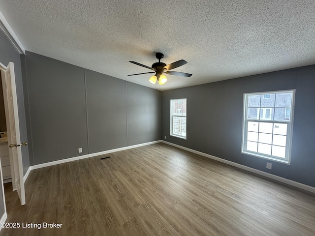 empty room featuring a ceiling fan, baseboards, wood finished floors, visible vents, and a textured ceiling