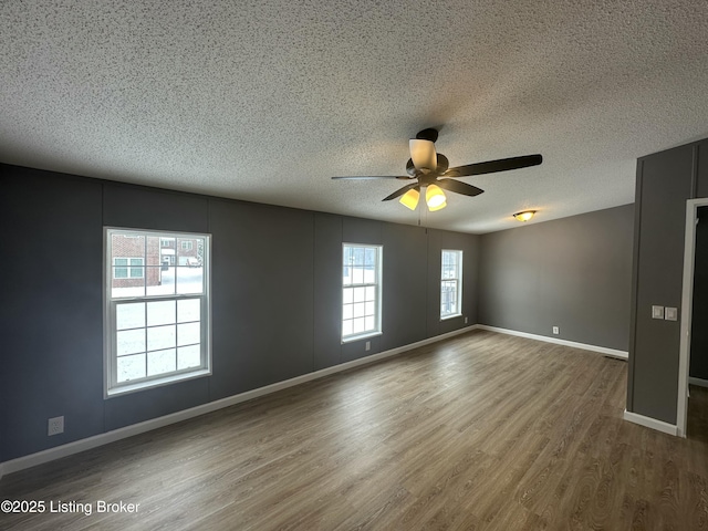 unfurnished room with a ceiling fan, wood finished floors, baseboards, and a textured ceiling