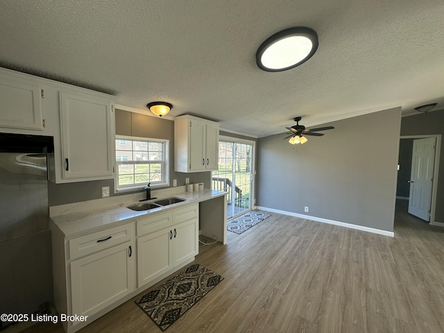 kitchen with baseboards, a sink, light wood-style floors, white cabinetry, and fridge