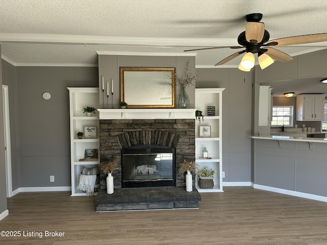 unfurnished living room featuring ornamental molding, a fireplace, wood finished floors, a textured ceiling, and a ceiling fan