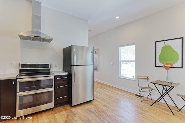 kitchen with light hardwood / wood-style floors, dark brown cabinets, stainless steel appliances, and range hood