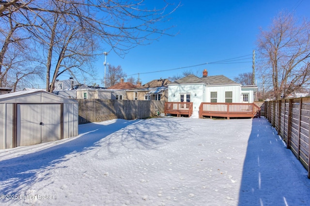 yard layered in snow featuring a storage shed and a wooden deck