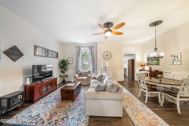 living room with ceiling fan with notable chandelier, a textured ceiling, dark hardwood / wood-style flooring, and a wood stove