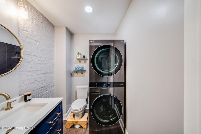 laundry area with wood-type flooring, stacked washing maching and dryer, and sink