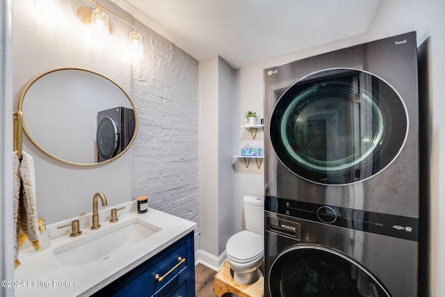 bathroom featuring stacked washer / dryer, hardwood / wood-style floors, vanity, and toilet