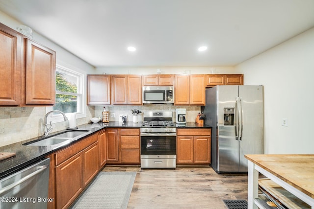 kitchen with dark stone counters, sink, decorative backsplash, light hardwood / wood-style floors, and stainless steel appliances