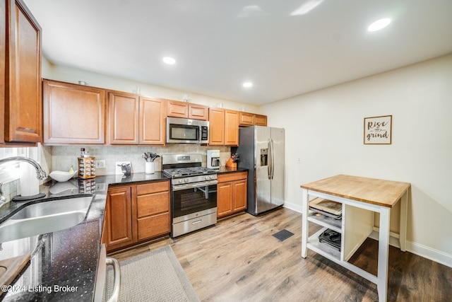 kitchen with sink, decorative backsplash, dark stone countertops, light wood-type flooring, and stainless steel appliances