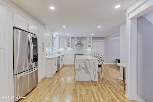 kitchen featuring a center island, wall chimney exhaust hood, stainless steel appliances, backsplash, and white cabinets