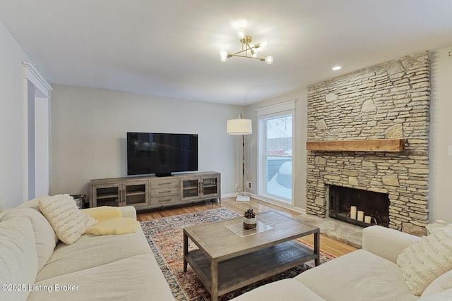 living room featuring hardwood / wood-style flooring, a notable chandelier, and a stone fireplace