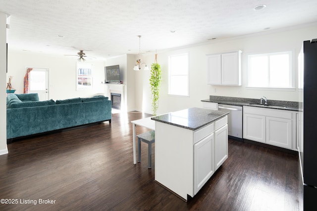 kitchen featuring a center island, white cabinetry, stainless steel dishwasher, ceiling fan with notable chandelier, and dark wood-type flooring