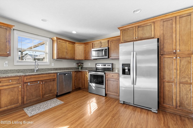 kitchen with stainless steel appliances, sink, light hardwood / wood-style floors, and stone counters