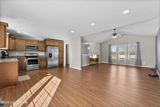 kitchen featuring vaulted ceiling, wood-type flooring, stainless steel appliances, ceiling fan, and sink