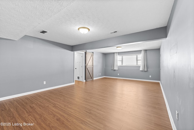 basement featuring hardwood / wood-style flooring, a textured ceiling, and a barn door