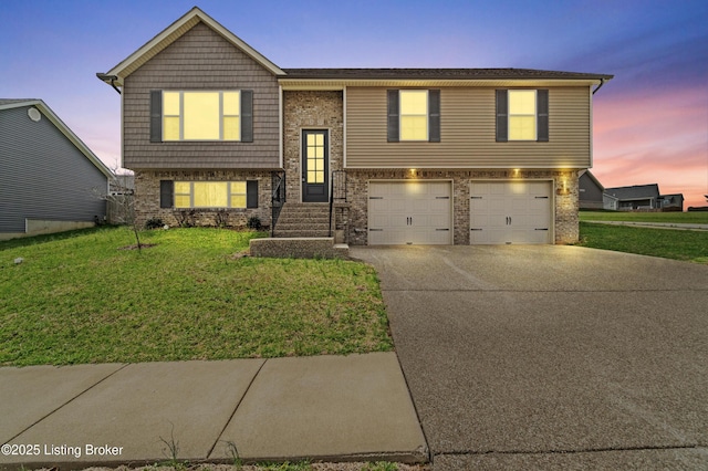 bi-level home featuring concrete driveway, a garage, brick siding, and a yard