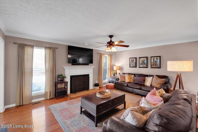 living room with crown molding, ceiling fan, light hardwood / wood-style flooring, and a textured ceiling