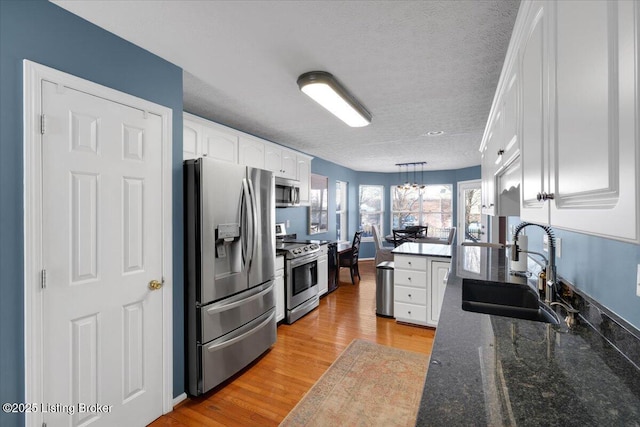 kitchen featuring pendant lighting, sink, light hardwood / wood-style flooring, white cabinetry, and stainless steel appliances