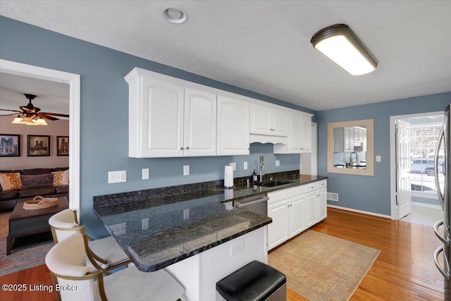 kitchen featuring sink, ceiling fan, white cabinetry, light hardwood / wood-style floors, and dark stone counters