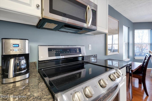 kitchen featuring white cabinetry, wood-type flooring, a textured ceiling, appliances with stainless steel finishes, and dark stone counters