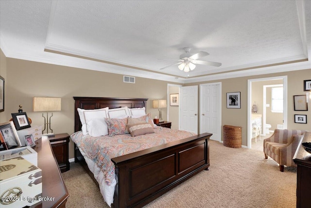 bedroom featuring crown molding, connected bathroom, a textured ceiling, light colored carpet, and a raised ceiling