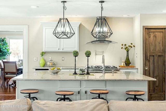 kitchen featuring light stone countertops, white cabinetry, a kitchen island with sink, a kitchen breakfast bar, and decorative light fixtures