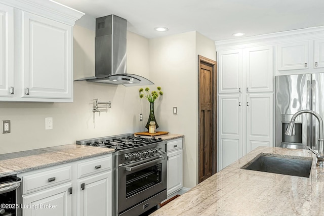 kitchen with wall chimney range hood, white cabinets, sink, stainless steel appliances, and light stone counters