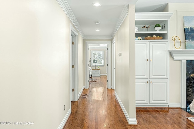 hallway with wood-type flooring, built in features, and ornamental molding