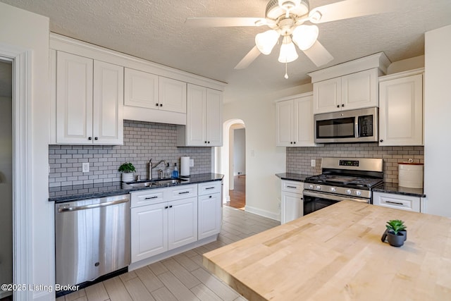 kitchen with stainless steel appliances, white cabinetry, sink, and wooden counters