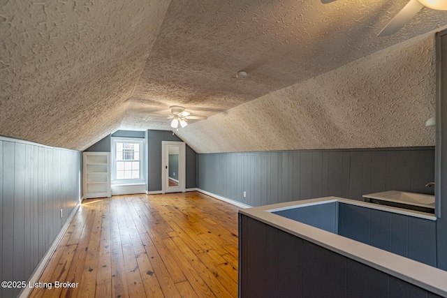 additional living space with ceiling fan, vaulted ceiling, a textured ceiling, and light wood-type flooring