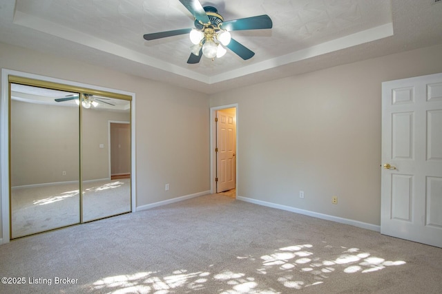 unfurnished bedroom with ceiling fan, light colored carpet, a tray ceiling, and a closet