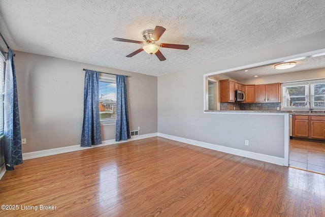 unfurnished living room with light hardwood / wood-style floors, plenty of natural light, a textured ceiling, and ceiling fan