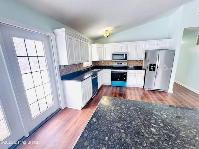 kitchen with white cabinets, vaulted ceiling, backsplash, and stainless steel appliances