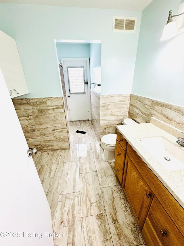 bathroom with toilet, vanity, and tile walls