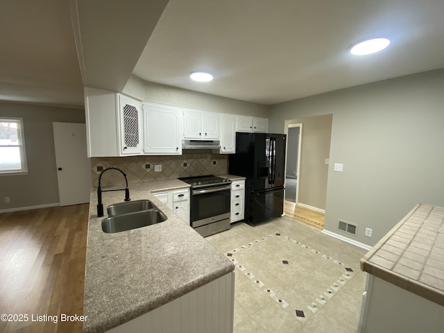 kitchen with backsplash, black fridge, sink, white cabinetry, and stainless steel range with electric cooktop