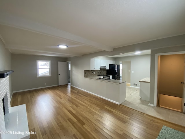 unfurnished living room featuring sink, beamed ceiling, light hardwood / wood-style flooring, and a brick fireplace