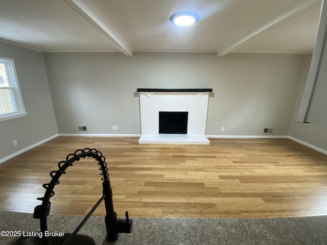 unfurnished living room featuring beam ceiling, wood-type flooring, and a brick fireplace