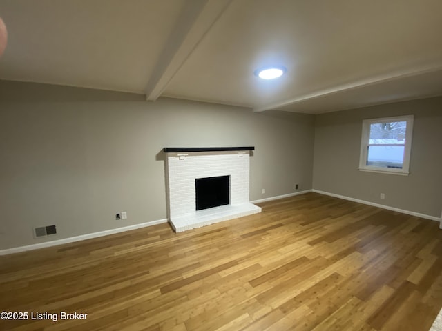 unfurnished living room with a fireplace, beamed ceiling, and hardwood / wood-style flooring