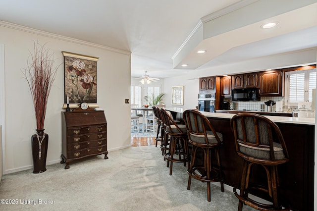 kitchen with a breakfast bar, ceiling fan, wall oven, and light colored carpet